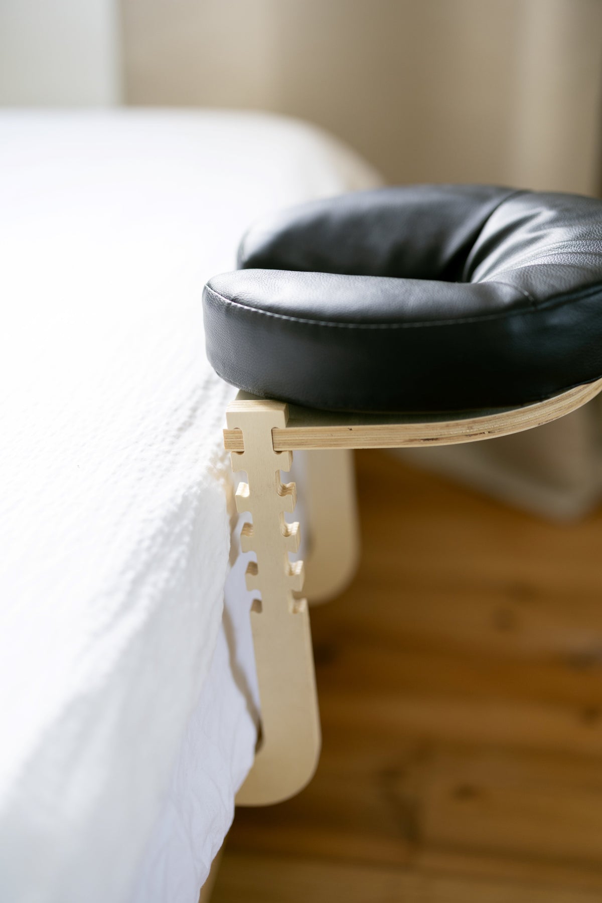 Den svarta huvudkudden på trästativet vid kanten av en bäddad säng
